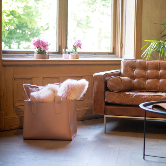 Kaminholztasche aus Leder in Old Pink steht neben Ledersofa und Blumen in stilvoller, heller Altbauwohnung